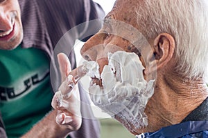 Old man getting his beard shaved by young skilled man at home