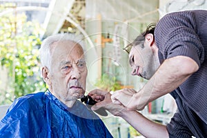 Old man getting his beard shaved by young skilled man at home