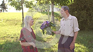 Old man gives flowers to his beloved wife in park.