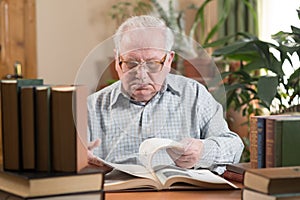 Old man in glasses reading a books in the room