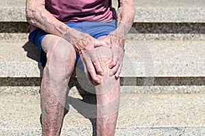 Old man with gnarled hands clutching his knee