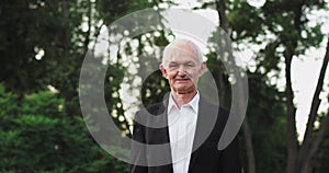 Old man grandfather looking straight to the camera , at nature in a black suit smiling a bit