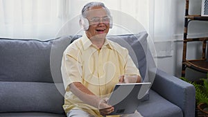 Old man grandfather smile relaxing wear headphones is listening to music using a digital tablet
