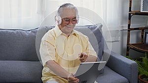 Old man grandfather smile relaxing wear headphones is listening to music using a digital tablet