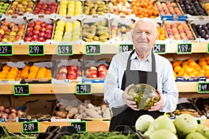 Old man green grocer worker standing with melon in hands