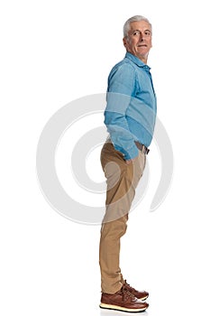 Old man with grey hair holding hands in pockets and looking behind