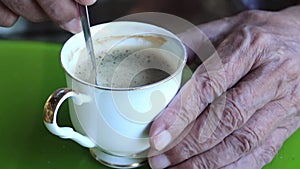 old man hands used spoon stirring coffee in white cup or mug on green table background