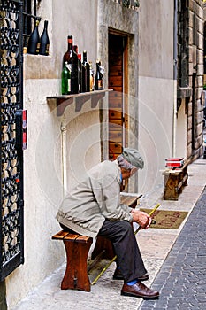 Old man with hat and cane sitting in front of a wine shop