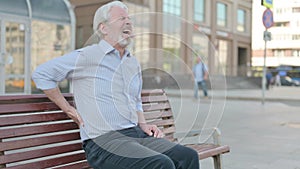 Old Man having Back Pain while Sitting on Bench Outdoor