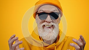 Old man having fun indoor. Joyful guy gesticulating on yellow studio background.