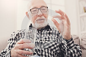 Old man having a glass of water and pills in hand