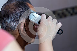 Old man having a hair cut by hairstylist using electrical battalion. men`s hairstyling and hair cutting with hair clipper in a bar