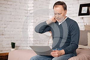 Old man having neckache while using laptop