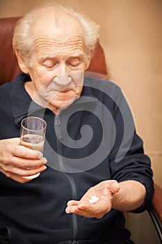 Old man holding a glass of water and pills