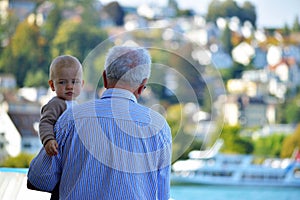 An old man holds a baby tenderly on boat trip from Interlaken West heading toward Thun City, Switzerland.