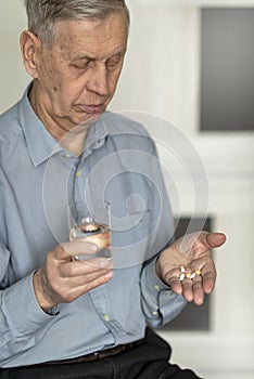 The old man holds pills and a glass of water in his hands.