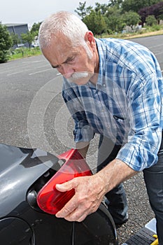 Old man installs tail light on vehicle
