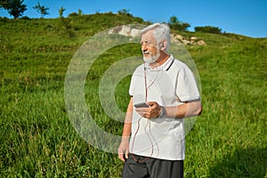 Old man keeping cellphone, standing on field looking at side.