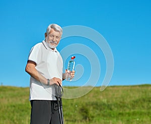 Old man keeping water bottle and tracking sticks.