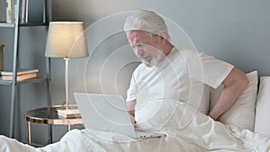 Old Man with Laptop having Back Pain in Bed