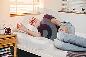 Old man lay in bed with hand holding pain in his legs alone at home