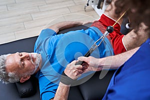 Old man laying and exercising in medical rehabilitation and physical therapy centr