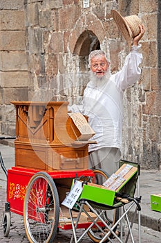 An old man with long white bread plays his street organ.