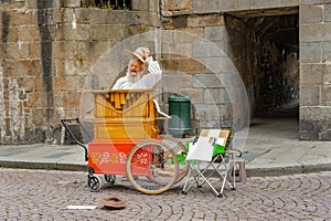An old man with long white bread plays his street organ
