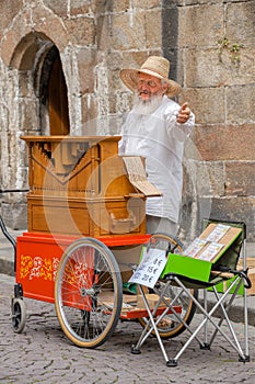 An old man with long white bread plays his street organ.