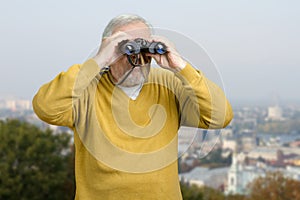 Old man looking through binocular on the city view.