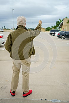 Old man looking for his car in a parking lot by pushing the unlock button on his fob