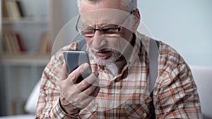 Old man looks incredulously at cellphone, new technology complicated for elderly