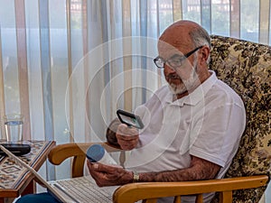 Old man  with magnifying glass reading on the jar with vitamines