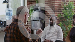 Old man making confession about alcoholism and depression in front of people at group therapy