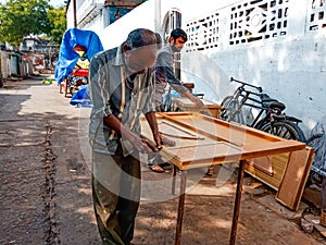 an old man making wooden furniture at open area workshop in India January 2020