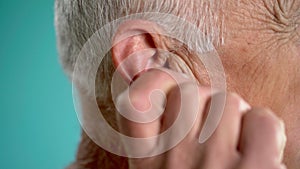 Old man massaging earlobe while standing on blue background