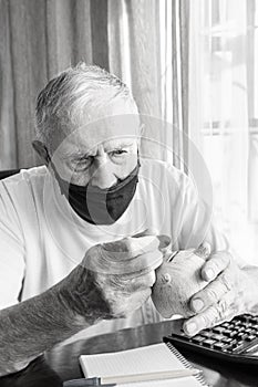 old man in a medical mask counts pennies from the pension fund. A worried elderly man puts money in a piggy bank. impact