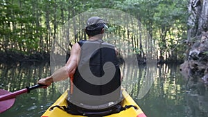 old man paddles on kayak in canyon among mangrove jungle