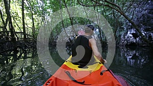 old man paddles on kayak in canyon among mangrove jungle