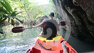 old man paddles on kayak in canyon among mangrove jungle