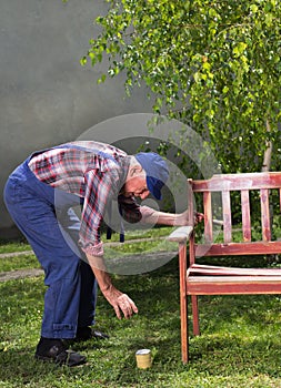 Old man painting bench in garden