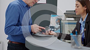 Old man paying checkup visit with credit card at hospital reception desk