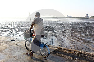Old man pedaling his bicycle on the beach in Surabaya, Indonesia