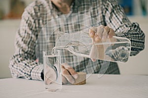 Old man pouring water from bottle to glass in kitchen