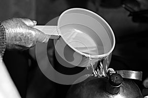 old man pours water from a bucket into a kettle, black and white photo