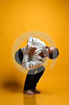 Old man practicing yoga doing stretching exercises against yellow background