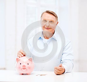 Old man putting coin into big piggy bank