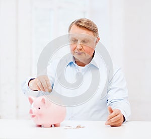 Old man putting coin into big piggy bank