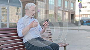 Old Man Reacting to Loss on Smartphone while Sitting Outdoor on Bench