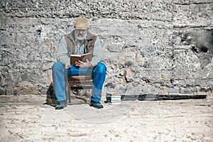 Old man reads a book, sits on an old chair, reads a book